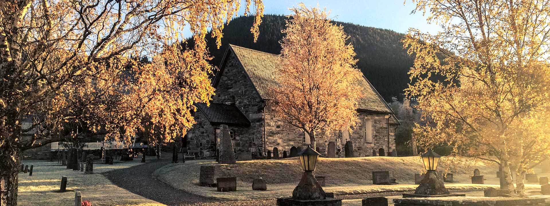Åre gamla stenkyrka från 1100-talet omgärdad av gula höstbjörnar med fjället Totthummeln i bakgrunden.