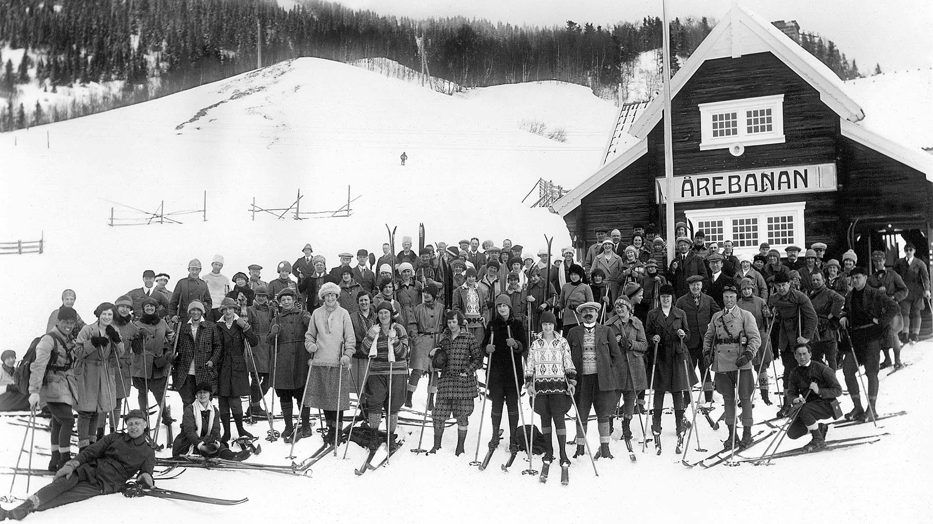 A group of people dressed in period clothing stands in front of the Åre Funicular. The photograph is in black and white.