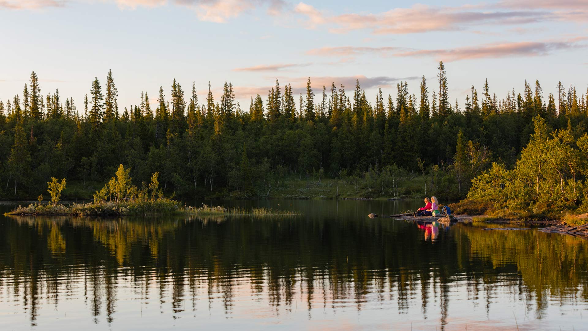 Two persons sitting by a lake a calm summer evening.