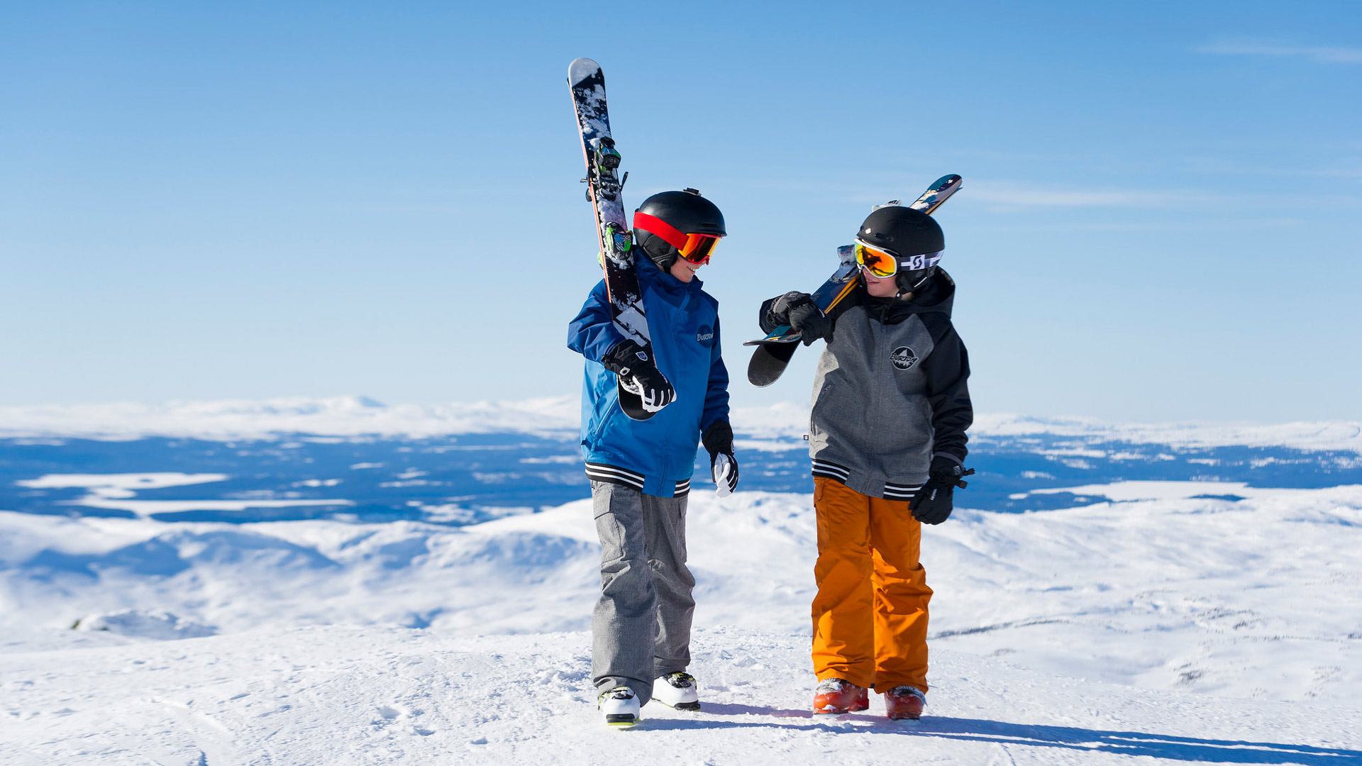 Två barn kommer gåendes med skidor en solig vinterdag
