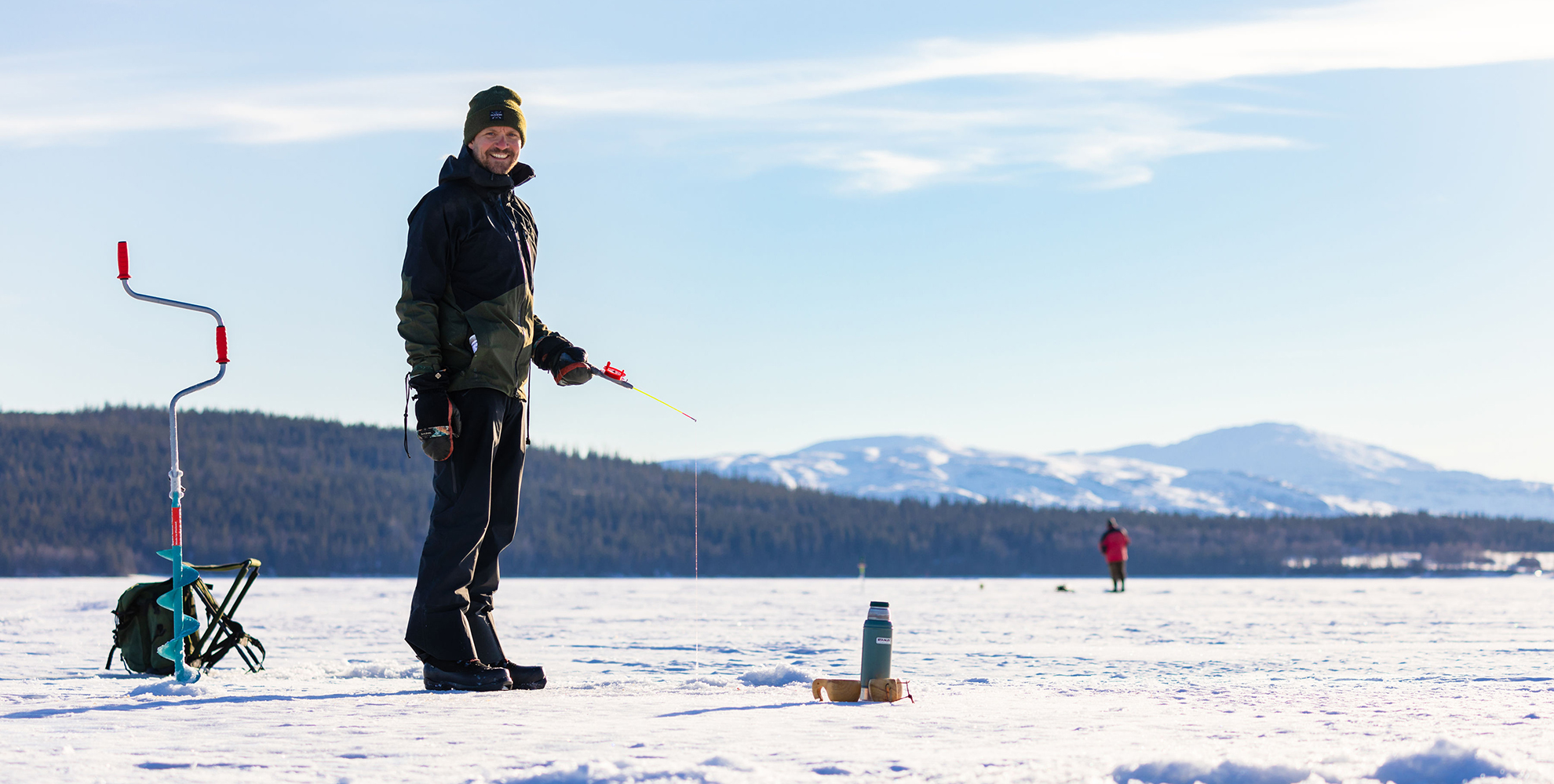 Man standing on the ice, fishing through the hole of a lake.