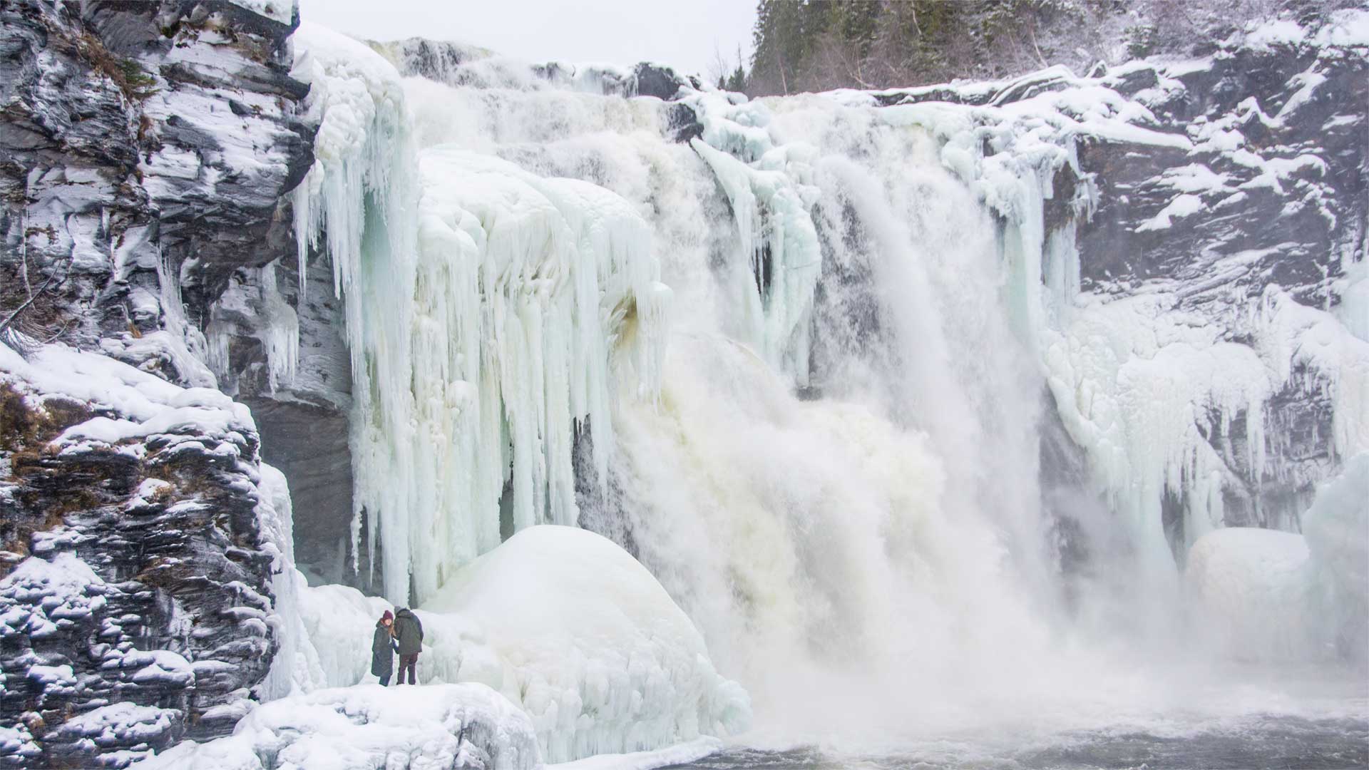 Two people standing beside Tännforsen at winter time.