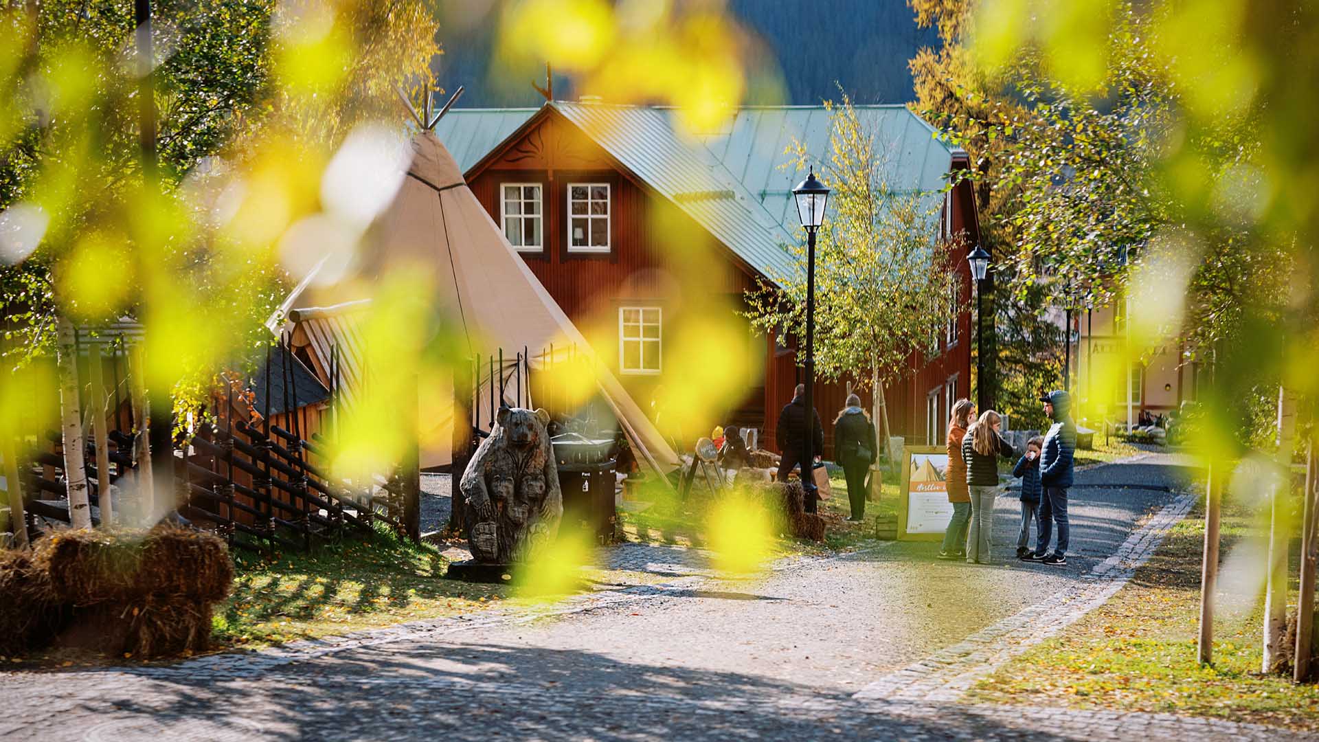 Ett tipitält framför ett rött hus med gröna löv i förgrunden från höstlov i Åre.