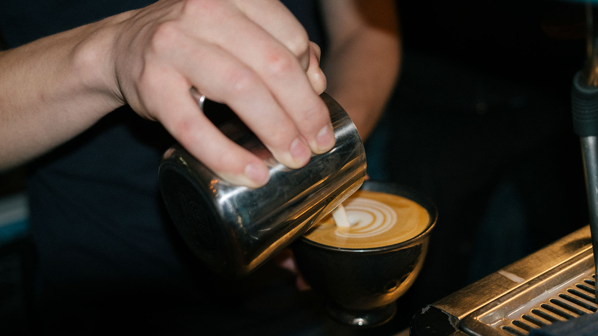 Närbild på baristas hand som gör latte art.