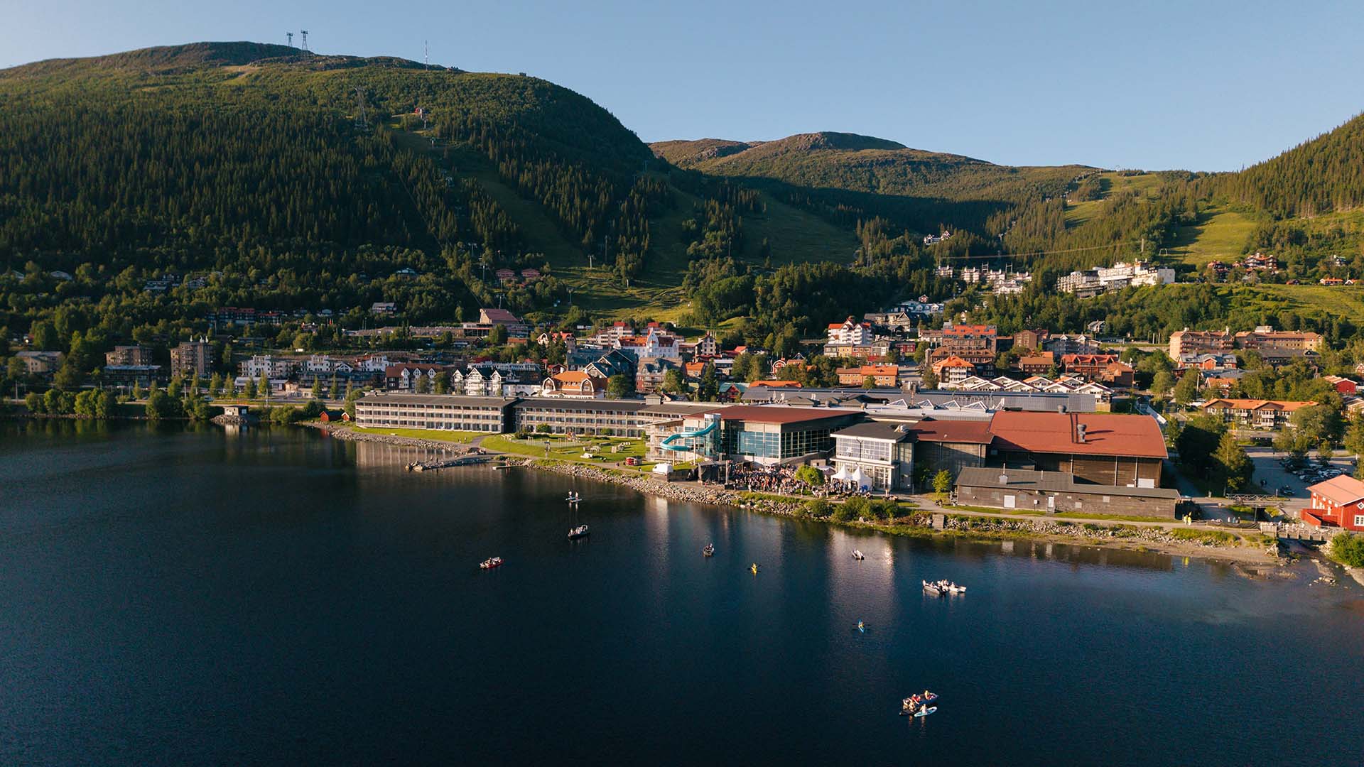 Flygfoto över Åresjön och Åre by, med båtar på vattnet och ett myller av människor vid Åresjöns strand.