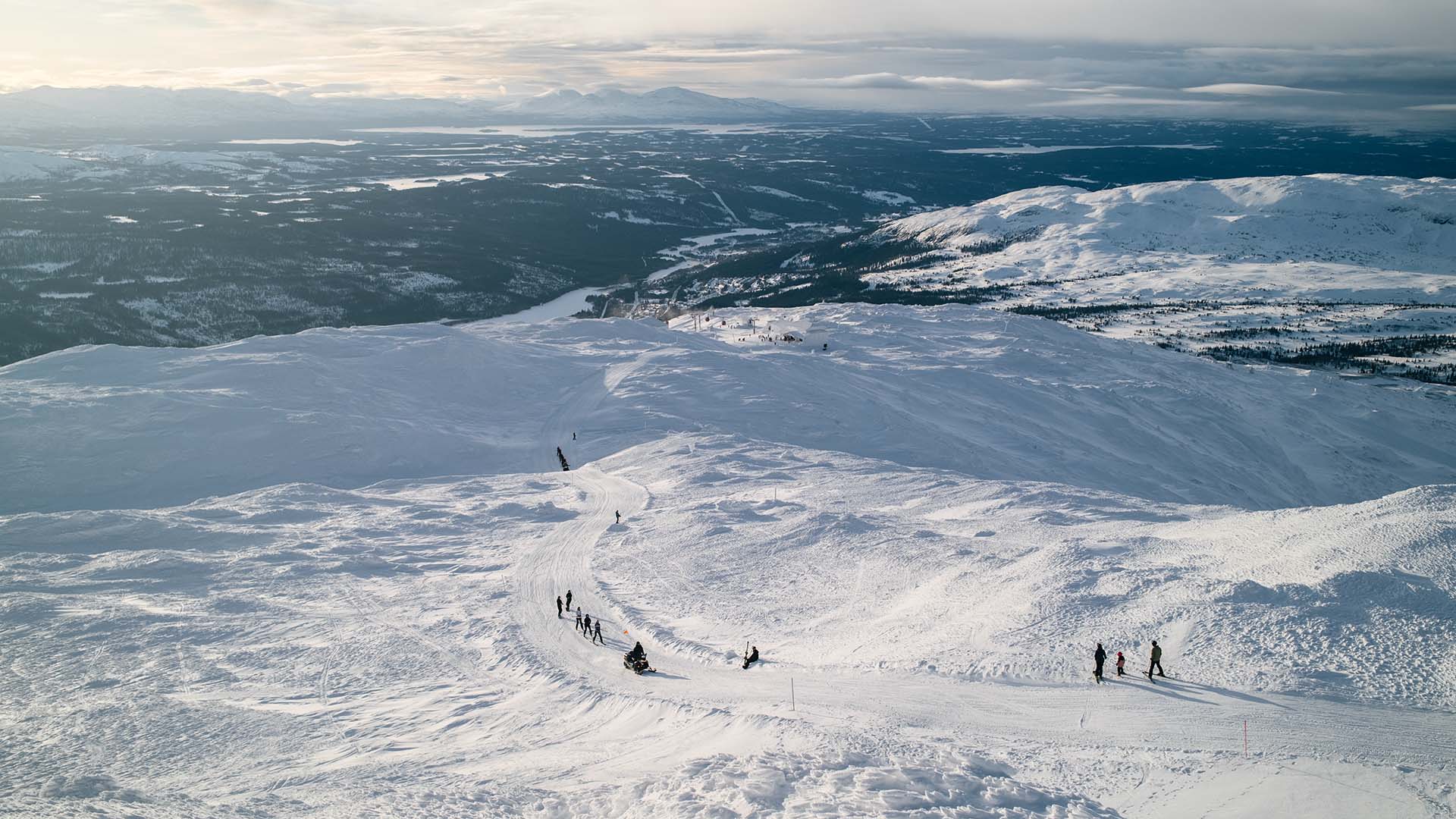 View of Åreskutan, with a snowmobile towing skiers across the snow.