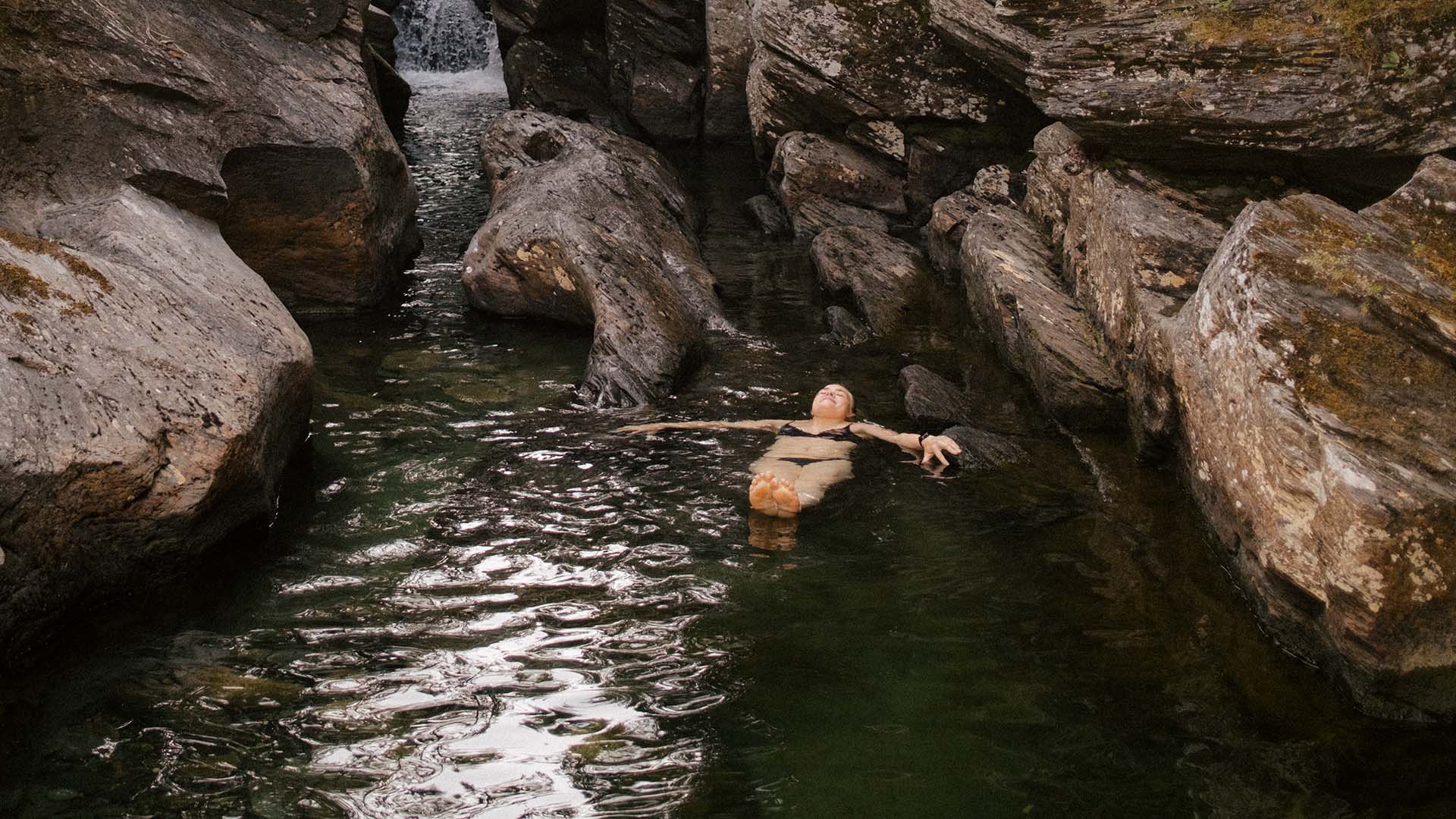 Kvinna ligger på rygg i vattnet i de naturliga kanjonerna i Ullån.