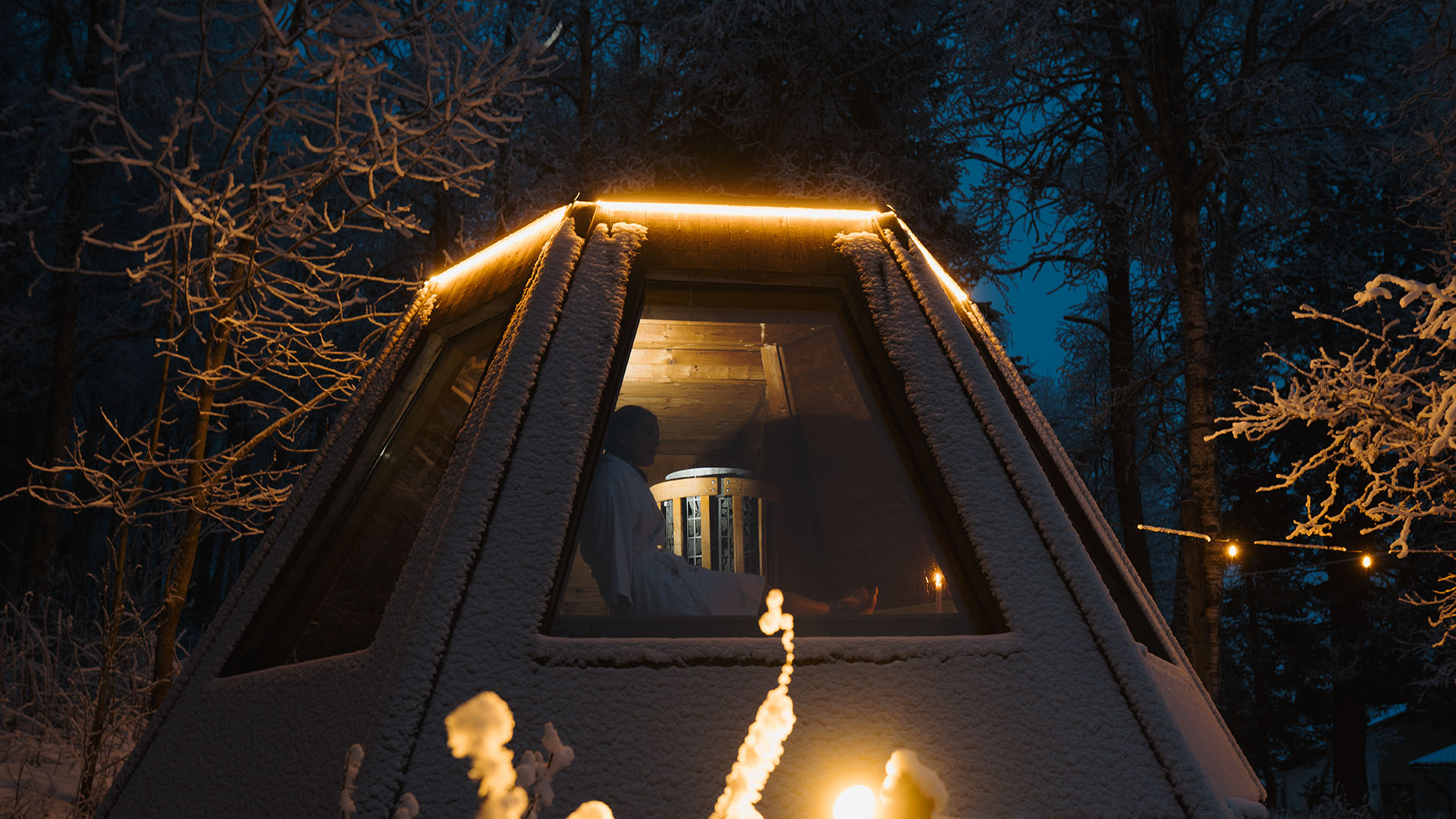Lit sauna under snow covered trees.
