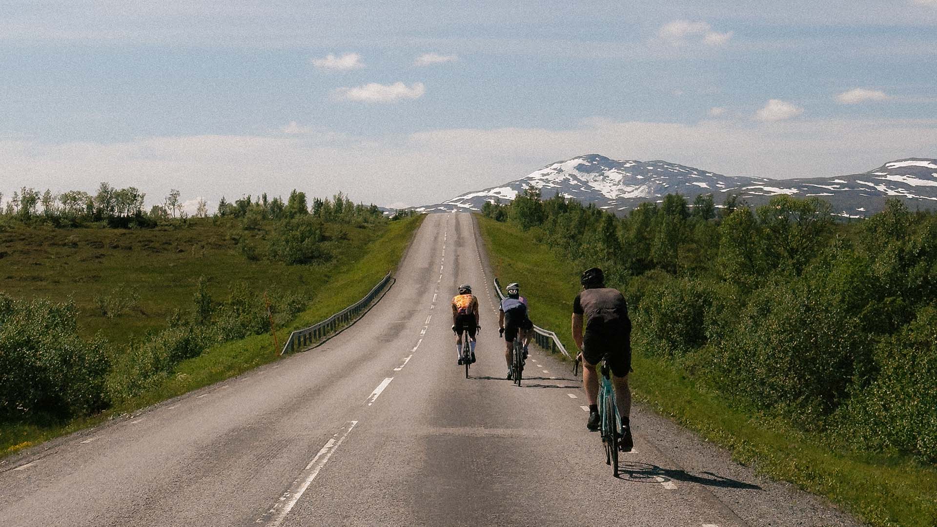 Landsvägscyklister på väg över Skalstugevägen med fjäll i bakgrunden.