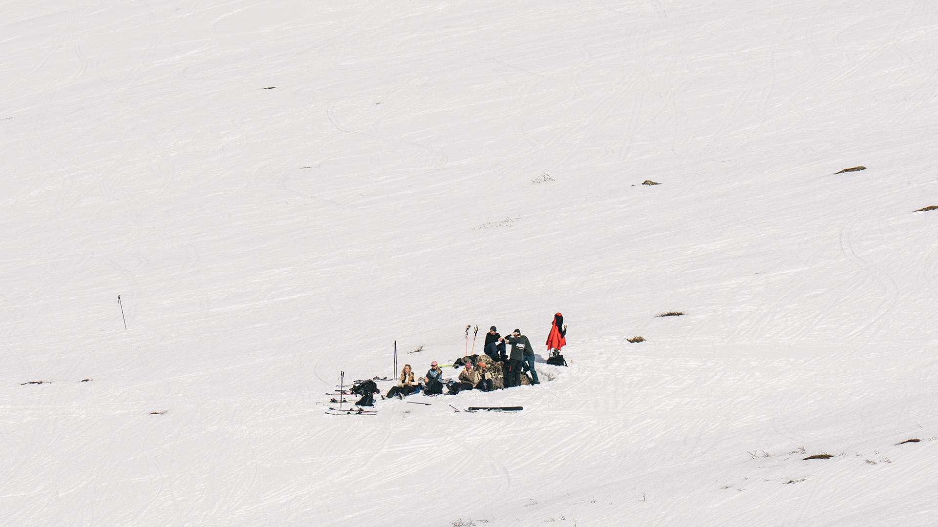 Mitt på fjällsidan sitter en grupp människor i solskenet och har byggt soffor av snö.
