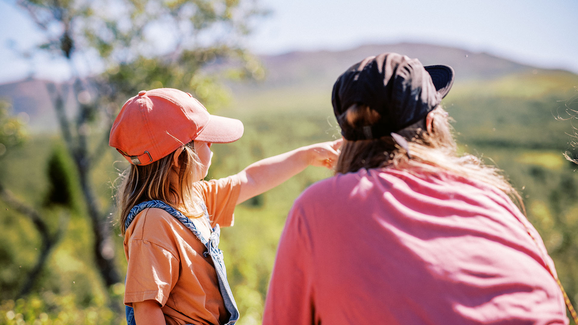 Ett barn pekar mot fjället och visar utsikten för sin mamma som sitter på huk bredvid.