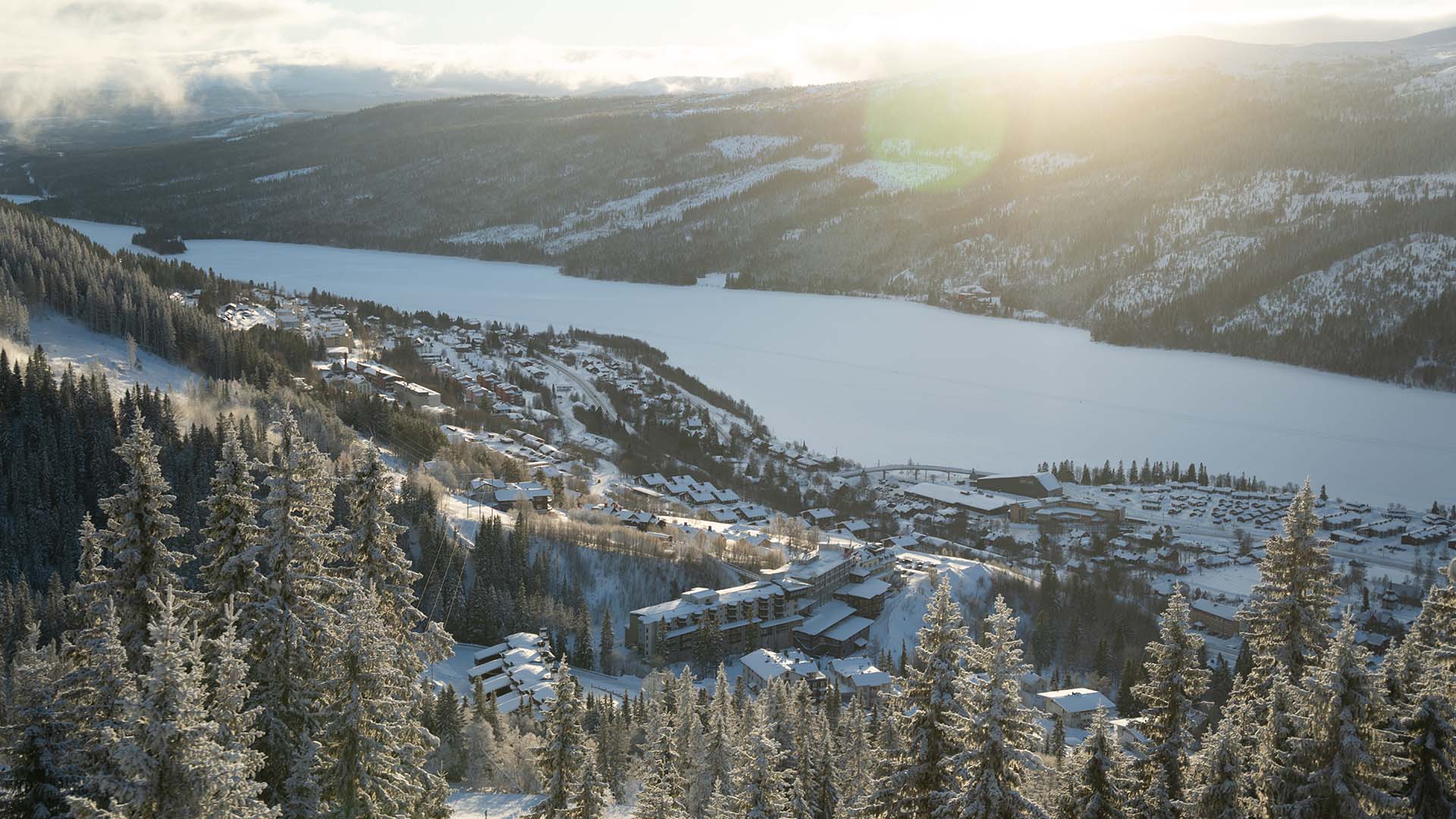 Bild som visar hela Åre by med snötäckta granar och Åresjön täckt av is och snö och byn med alla hus som syns långt bort.