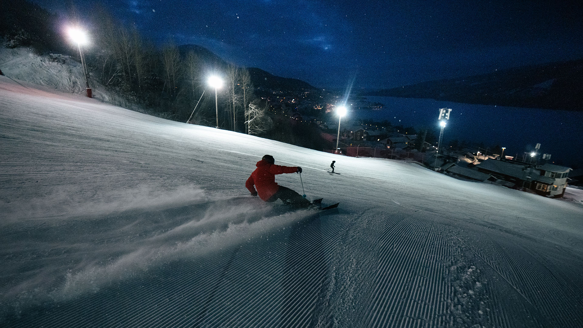 Skidåkare på kvällen i Åre med byn ljus i bakgrunden.